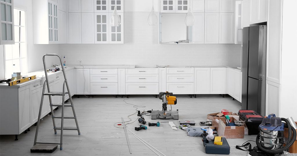 A kitchen remodeling process with white cabinets and tools on the floor