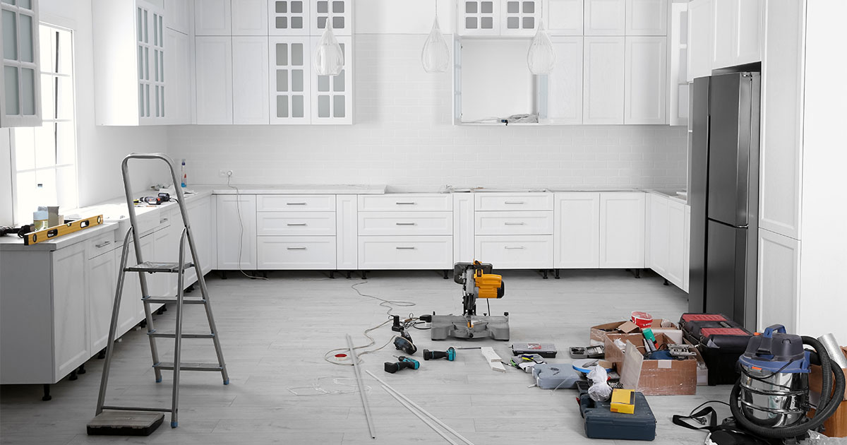 A kitchen remodeling process with white cabinets and tools on the floor