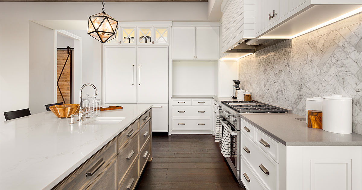 A kitchen with wood floors, beige kitchen island, and white cabinets with beige hardware