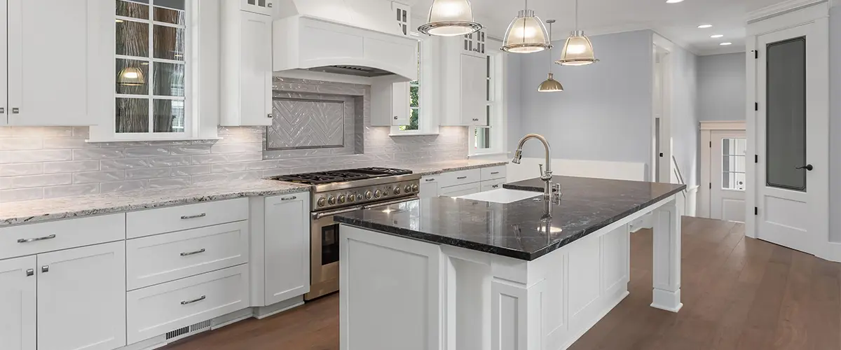 A kitchen with white cabinets and dark countertop on island
