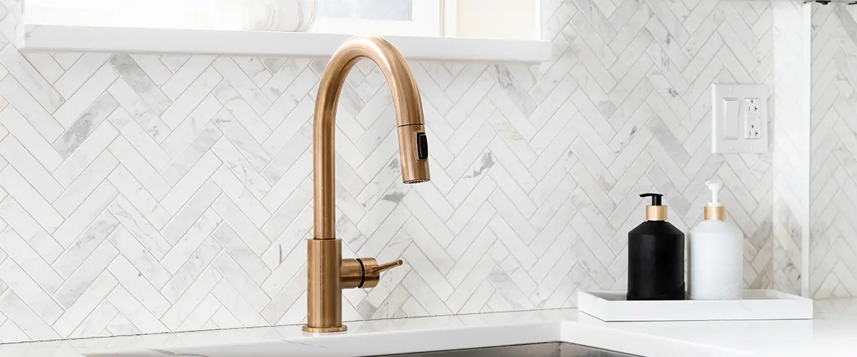 A golden faucet with beautiful tile backsplash