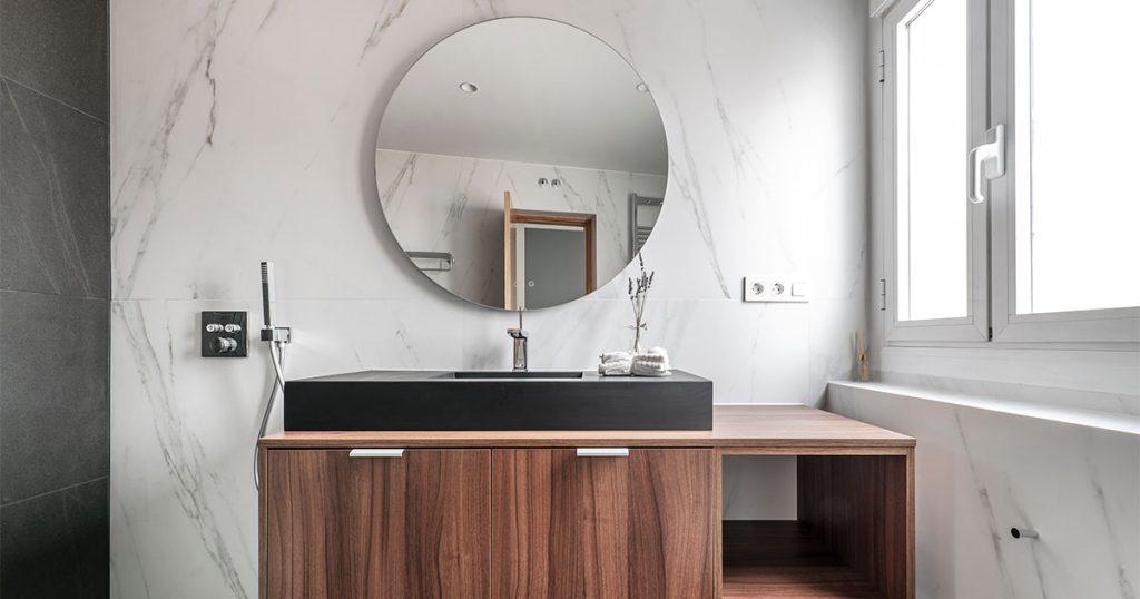A beautiful bathroom sink with a round mirror and a wood vanity