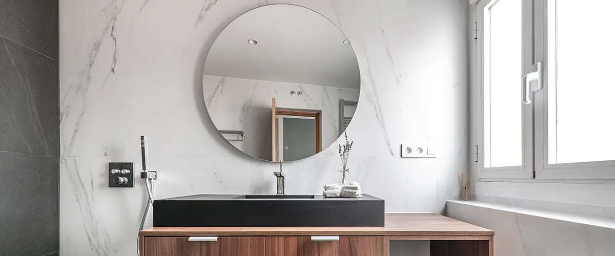 A beautiful bathroom sink with a round mirror and a wood vanity