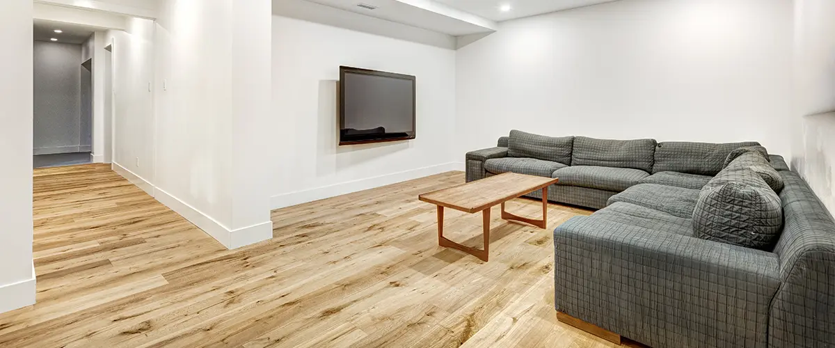 Wood flooring in a basement with a gray couch and a TV