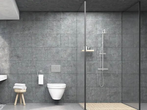 A bathroom with gray tile walls and flooring with a walk-in shower with glass panels