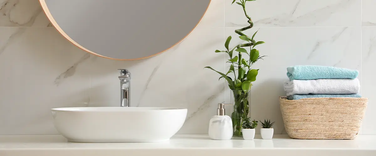 A vessel sink with a bamboo plant and folded towels