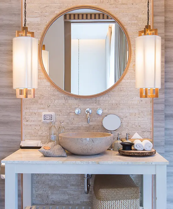 A round mirror with golden features and a bowl sink on a simple vanity